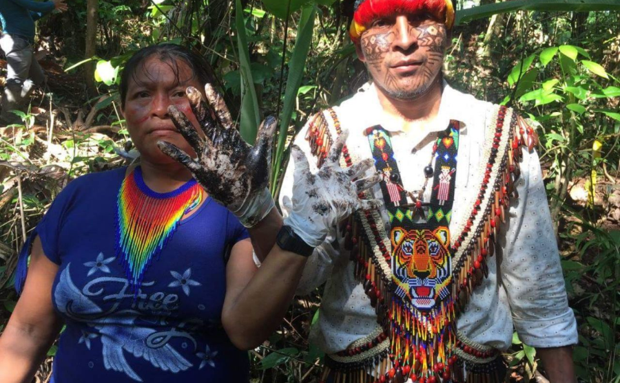 Isabel Wisum and an Achuar man holding up their hands covered in crude oil