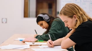 two teenage girls studying side by side at a table