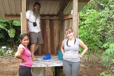 Two women and a man standing by a compost toilet in the jungle