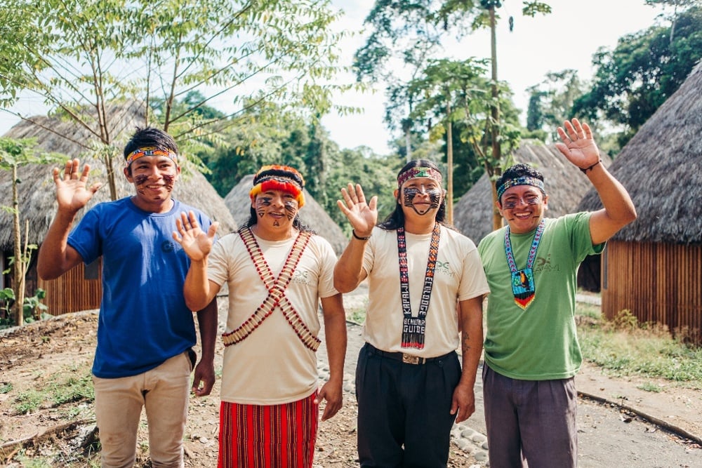 Four Achuar men smiling and waving 